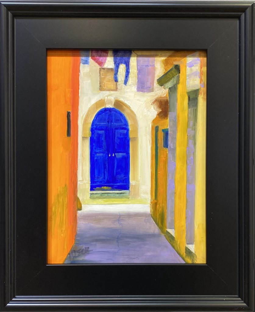 Framed oil painting titled 'Blue Door' by Henry Leck, featuring a vibrant blue arched door set within a sunlit alleyway lined with colorful Mediterranean-style buildings.